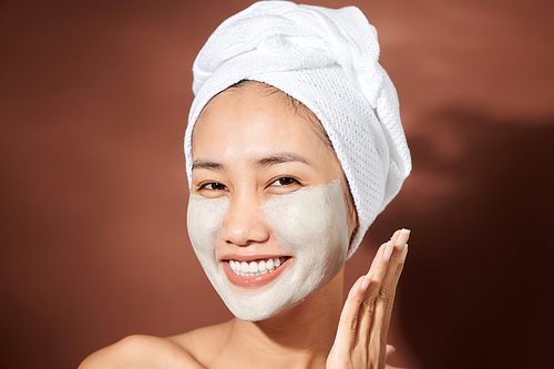 Smiling young Asian woman wearing white towel and has a facial mask.