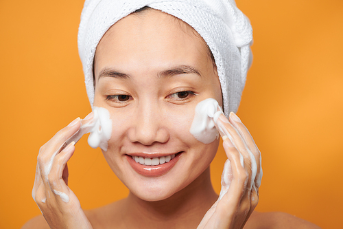Laughing girl applying moisturizing cream on her face. Photo of young girl with flawless skin on orange background. Skin care and beauty concept