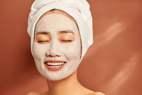 Young Asian woman with a white towel on her head and a clay mask on her face