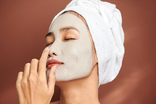 Close up shot of beautiful Asian woman applies purifying mask on face, has beauty treatments