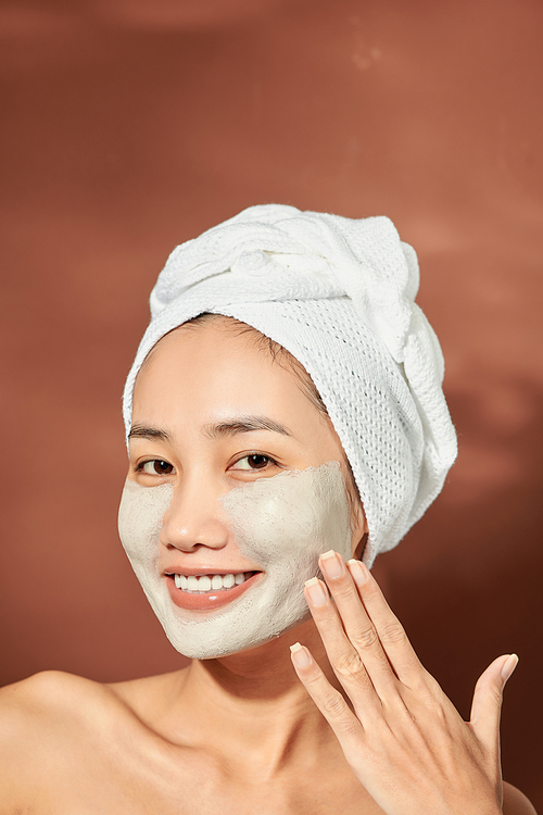 Emotional portrait of a happy and positive beautiful nude young woman with a clay cosmetic mask on her face