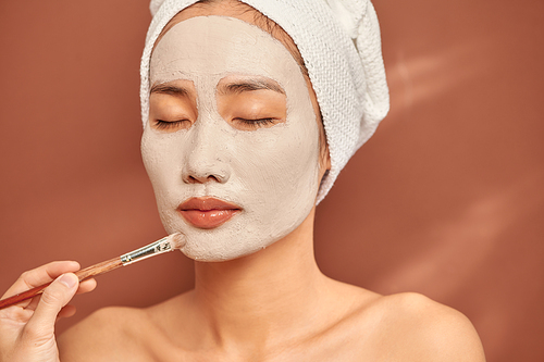 Spa Asian girl applying facial clay mask. Beauty treatments. Over blue background.