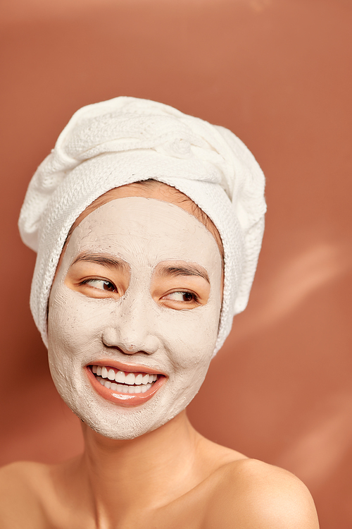 Close up portrait of charming Asian woman with a white towel on her head and clay mask on her face.