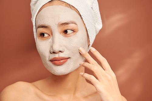 Attractive woman applying clay mask on her face.