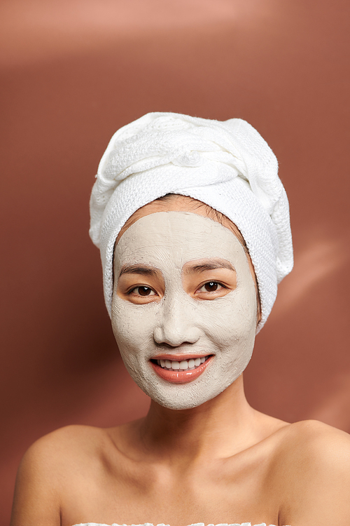 Portrait of young Asian wearing clay mask over brown background.
