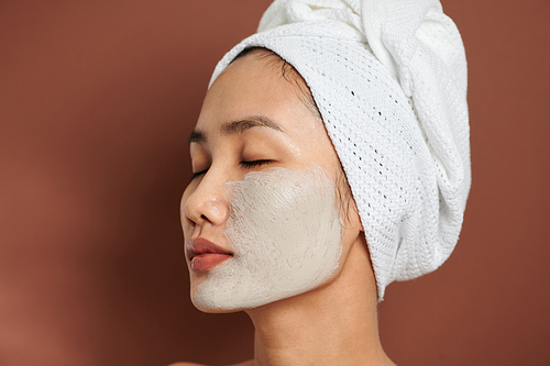 Close up shot of beautiful Asian woman applies purifying mask on face, has beauty treatments