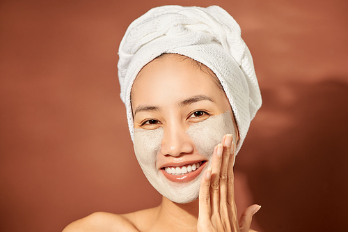 Beautiful cheerful Asian teen girl applying facial clay mask. Beauty treatments, isolated on light background.