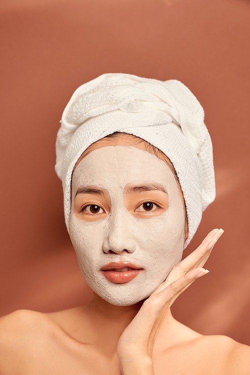 happy woman with a towel on her head apply a cleansing mask on her face