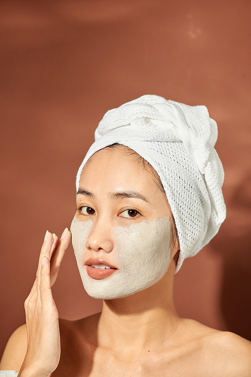 An attractive young Asian girl with a white towel on her head applied a useful clay mask