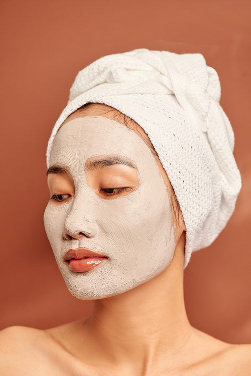 Close-up Portrait of beautiful Asian girl in spa with a towel on her head applying facial clay mask.
