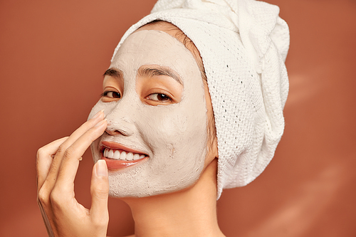 Beautiful Asian woman applying facial mask on her face. Skin care and treatment, spa, natural beauty and cosmetology concept.