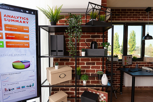 Close up of bookshelf with vase plants and decorations in business office. House plants, boxes, and modern objects on shelves to decorate startup workplace. Decorative accessories