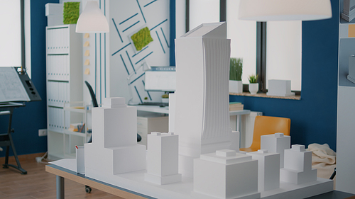 Concept of building model and construction design on table in empty workplace. Maquette and urban property plan used for real estate development. Architectural blueprints structure.