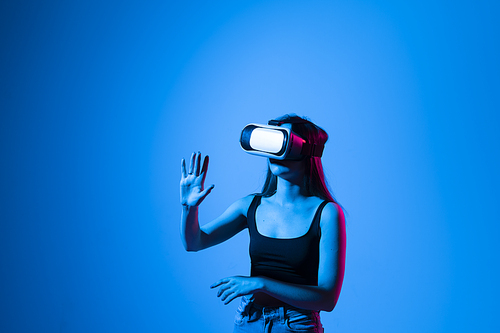 Close up of young woman stands in studio wearing VR glasses and swiping scrolling zooming with hands in a virtual space while interacting with a objects in a metaverse. Virtual reality technology