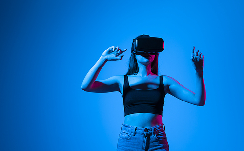Young woman using the virtual reality headset and interact with a virtual world in a metaverse. Female model wearing VR goggles