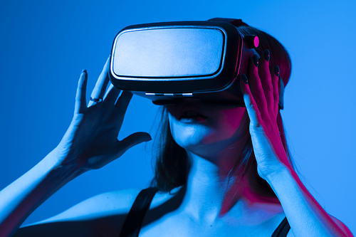 Young woman using VR headset helmet to interacts with metaverse using swipe and stretching gestures. Watching virtual reality 3d video. Girl in VR goggles looking around