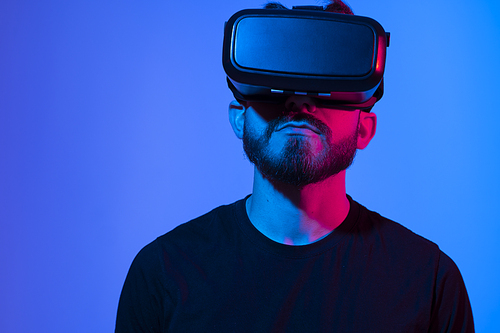 Bearded man using VR headset helmet to interacts with metaverse using swipe and stretching gestures. Watching virtual reality 3d video. Man in VR goggles looking around