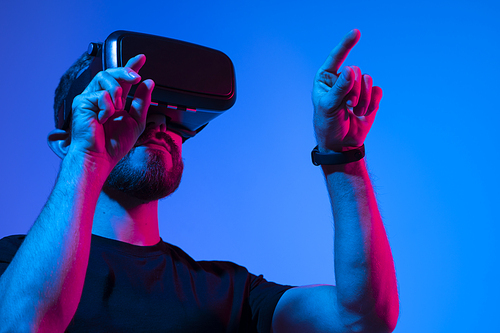 Young bearded man in virtual reality helmet plays online game in metaverse. Game simulates behavior in fictional world, gadgets and virtual reality addiction. Future technology concept
