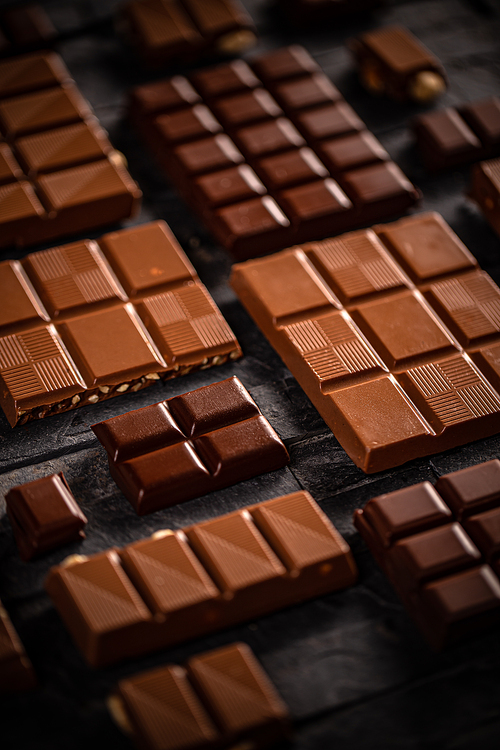 Sweet milk and hazelnut chocolate bar pieces on black background
