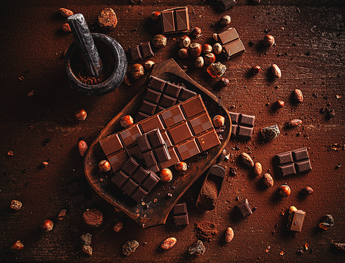 Cocoa powder, beans and chocolate bar pieces on dark wooden background.