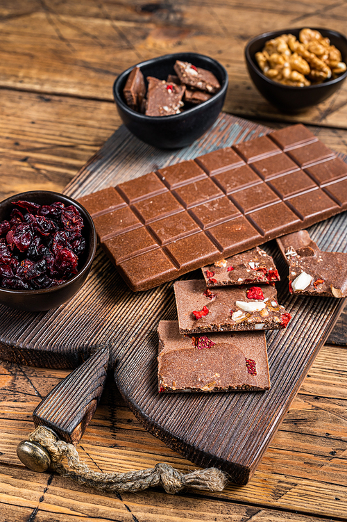 Dark chocolate bar with hazelnuts, peanuts, cranberries and freeze dried raspberries on a wooden board. wooden background. Top view.