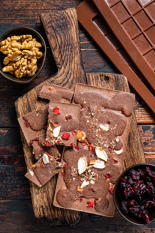 Homemade Craft milk chocolate bar with hazelnuts, peanuts, cranberries and freeze dried raspberries. Dark wooden background. Top view.