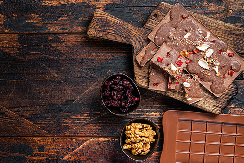 Homemade Craft milk chocolate bar with hazelnuts, peanuts, cranberries and freeze dried raspberries. Dark wooden background. Top view. Copy space.