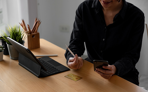 Happy woman holding credit card and using laptop and smartphone. Online shopping, booking and banking concept. Businesswoman or entrepreneur in the home office.