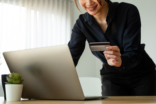 Young woman holding credit card and using laptop computer at home. Online shopping, e-commerce, internet banking, spending money