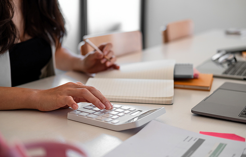 Business woman with calculator counting making notes at office hand is writes in a notebook at home office.