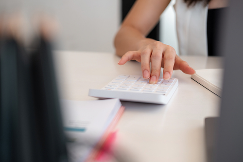 Close up woman hand using calculator and writing make note with calculate about cost at home office.