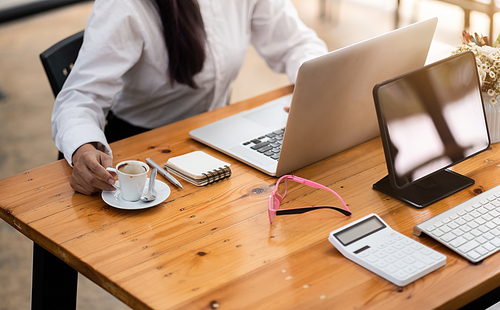 Accounting woman using laptop computer on workplace table with digital tablet and calculator at cafe.