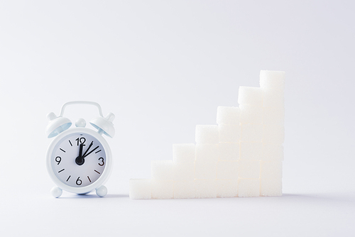 Ascending stacks of sugar cubes graph chart and alarm clock, studio shot isolated on white background, health high blood risk of diabetes concept