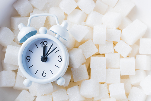 Sugar cube texture background sweet food ingredient and alarm clock, studio shot health high blood risk of diabetes, and calorie intake concept