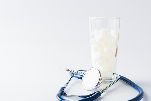 A glass full of white sugar cube sweet food ingredient and doctor stethoscope, studio shot isolated white background, health high blood risk of diabetes and calorie intake concept and unhealthy drink