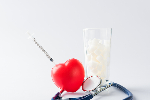 A glass full of white sugar cube sweet food ingredient and doctor stethoscope, studio shot isolated on white background, health high blood risk of diabetes and calorie intake concept and unhealthy drink