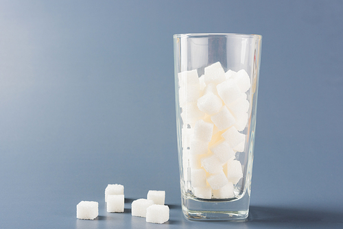 A glass full of white sugar cube sweet food ingredient, studio shot isolated on a gray background, health high blood risk of diabetes and calorie intake concept and unhealthy drink