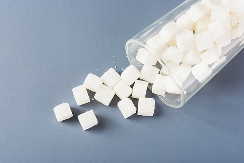 White sugar cube sweet food ingredient spilled out of the glass, studio shot isolated on a gray background, Minimal health high blood risk of diabetes and calorie intake concept