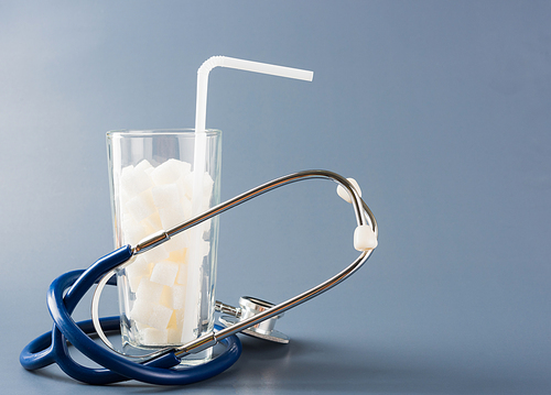 A glass full of white sugar cube sweet food ingredient and doctor stethoscope, studio shot isolated gray background, health high blood risk of diabetes and calorie intake concept and unhealthy drink