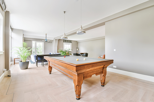 A room with a large wooden pool table and several windows on the wall