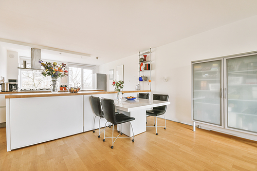 Modern minimalist style interior design of studio apartment with open white kitchen, and dining zone with table and chairs