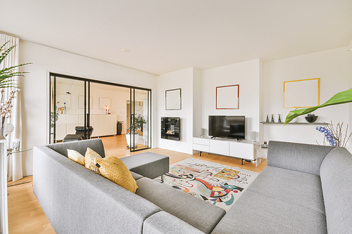 Interior of light living room with stylish sofa and decorations and glass door and windows leading to balcony on sunny day