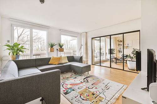 Interior of light living room with stylish sofa and decorations and glass door and windows leading to balcony on sunny day