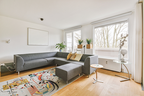 Interior of light living room with stylish sofa and decorations and glass door and windows leading to balcony on sunny day