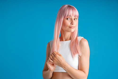 Young woman touching her smooth natural long pink dyed hair and looking surprised, posing isolated over blue studio background. Beauty, hair care concept