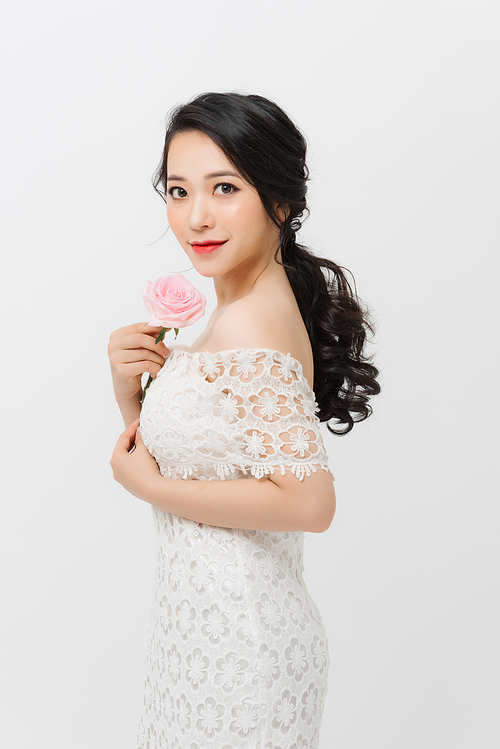 Attractive elegant Asian woman holding flower and wearing white dress over white background.