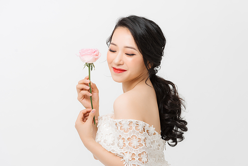 Profile portrait of a beautiful young woman smelling pink rose, isolated on white background.