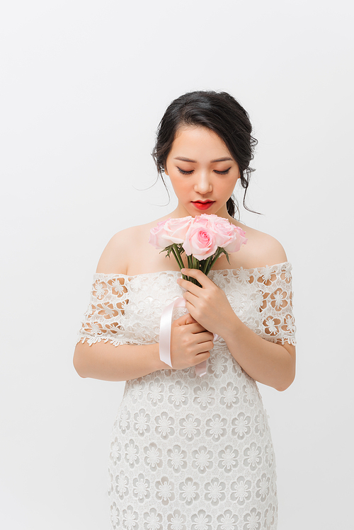 Profile portrait of a beautiful young woman smelling pink rose and looking down, isolated on white background.