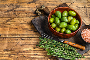 Marinated Green big olives in wooden bowl with oil. wooden background. Top view. Copy space.