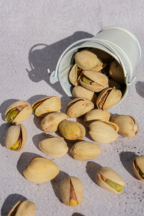 Pistachios in white bucket on concrete background. Healthy and dietary nutrition. Concept of nuts. Vegan protein omega vitamin food. Roasted salty pistachio. Harvest